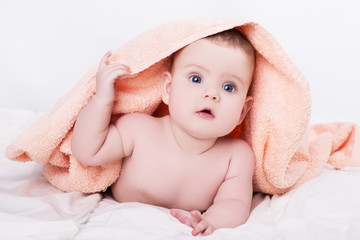 Surprised baby with big blue eyes lying on belly under the pink towel after bath