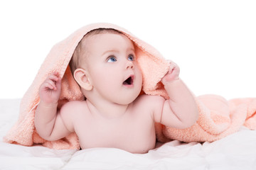 Surprised baby with big blue eyes lying on belly under the pink towel after bath