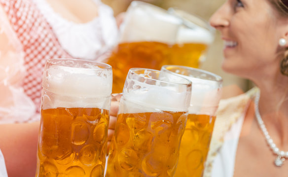Close-up of waitress in Bavarian clothes serving beer in five beer glasses to two women