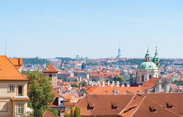 Obraz premium View across orange rooftops of Prague and city buildings under blue sky.