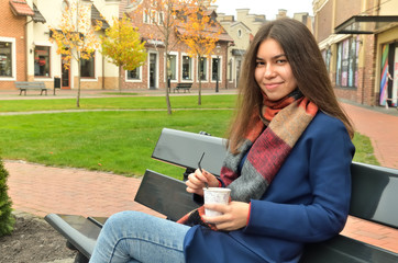 Fototapeta premium Asian girl sits on a bench outdoor with a cup of coffee