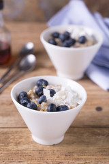 Steel cut oats with blueberries and coconut flakes served in a modern white bowl. Healthy eating concept