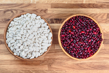 Beans red and white in a wooden bowl standing on the kitchen table made of oak. Top view.