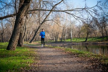 Young Sports Man Running in the Park in Cold Sunny Autumn Morning. Healthy Lifestyle and Sport Concept.
