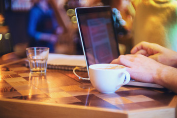 Closeup of cup of coffee and man's hand working on a laptop, working concept,