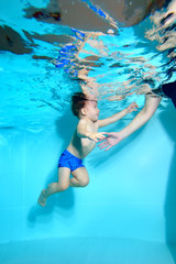 Happy kid swimming underwater to his mother. Portrait. Vertical orientation. The view from under the water