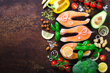 Uncooked salmon fish fillet with aromatic herbs, onion, avocado, broccoli, pepper bell, vegetables on wooden background, top view. Ingredients for cooking on background.