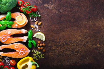 Uncooked salmon fish fillet with aromatic herbs, onion, avocado, broccoli, pepper bell, vegetables on wooden background, top view. Ingredients for cooking on background.