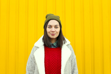 Millenial girl im fashionable clothes having a good time, making funny faces near bright yellow urban wall.