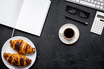 Morning of businessman. Coffee and croissants for breakfast near keyboard and notebook. Black background top view copy space