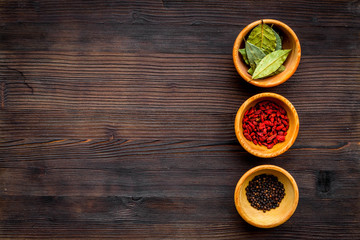 Template for menu design. Empty space near bowls with goji, bay leaf, pepper on dark wooden background top view copy space