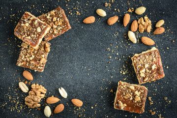 Homemade caramel shortbread squares cookies with nuts on black background with crumbs.