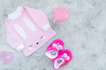 Cute pink baby clothes for girl. Shirt, booties, toy, bottle on grey background top view copy space
