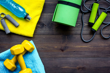 Fitness equipment. Jump rope, dumbbells, expander, mat, water on dark wooden background top view copy space