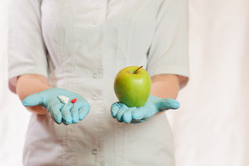 A medic girl holds in one hand red and white tablets, in another green apple