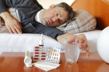 Mann krank im Bett nimmt Medikamente