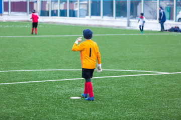 kid - goalkeeper plays football on the stadium at winter