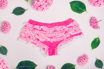 Top view Female sexy lace pantie and pink wisteria flowers and green leaves on the white background. Lingerie, beautiful underwear clothing. Fashion concept.
