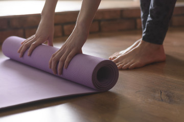 A barefoot woman twists a purple yoga Mat and fitness on the parquet floor