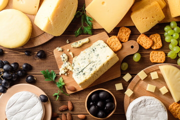 Various types of cheese on dark rustic wooden background.