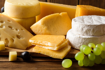 Various types of cheese on dark rustic wooden background.