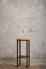 High metal bar chair with wooden seat near grunge concrete wall