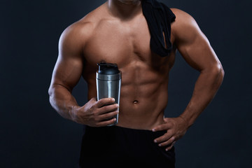 Naklejka premium Muscular bodybuilder with shaker bottle on black background.Strong athletic man shows body,abdominal muscles,chest muscles,biceps and triceps.Work out,gaining weight. Bodybuilding concept.