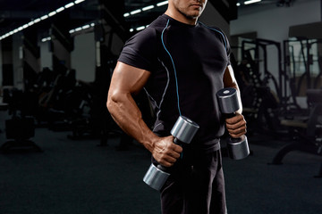 Muscular bodybuilder doing exercises with dumbbell in gym.Strong athletic man shows body,abdominal muscles,biceps and triceps.Work out,gaining weight,pumping up muscles with dumbbells.