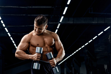Fototapeta na wymiar Muscular bodybuilder doing exercises with dumbbell in gym.Strong athletic man shows body,abdominal muscles,biceps and triceps.Work out,gaining weight,pumping up muscles with dumbbells.