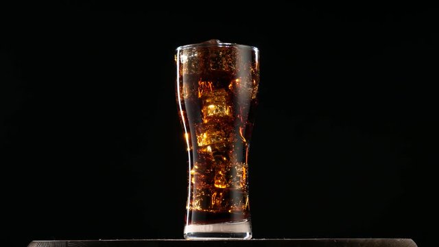 Cola with ice. Large glass of cold coke with ice cubes rotating.