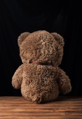 A lone Teddy bear sits on a wooden surface,