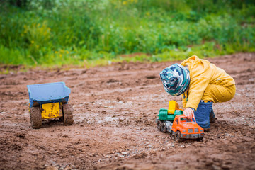 the boy in yellow suit playing with a toy car in the dirt