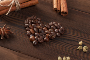 Coffee beans in the shape of heart with various spices on a wooden background