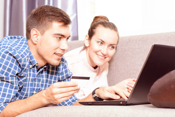 Modern young family makes purchases online Leda on sofa using a laptop, payment by credit card....