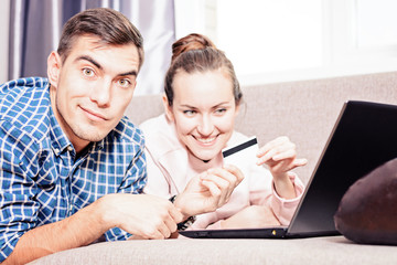 Modern young family makes purchases online Leda on sofa using a laptop, payment by credit card....