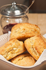 Close up of  four freshly baked, homemade, warm, buttermilk biscuits in a deep, square bowl, with a vintage jam glass with putter top and spoon  on a table