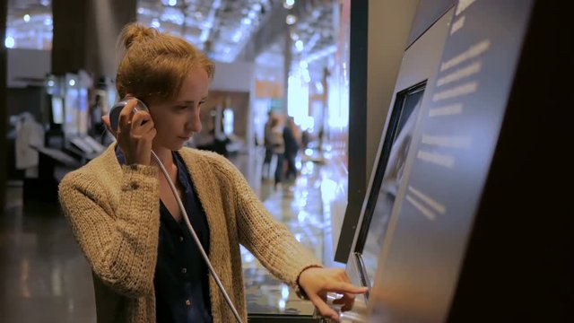 Woman touching interactive display, using headphones and listening audio guide at modern jewish history museum. Education and technology concept