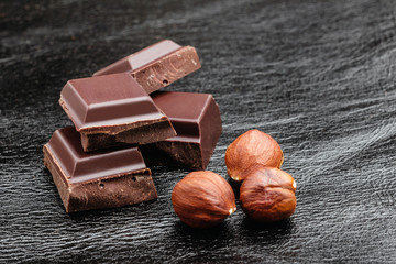 Pieces of bitter dark chocolate cubes with hazelnut on black leather texture background