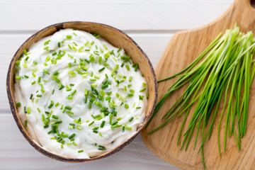Bowl of cream cheese with green onions, dip sauce on wooden table.