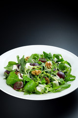 Fresh green salad with feta cheese, walnut and grapes , vertical close up shot on the dark background