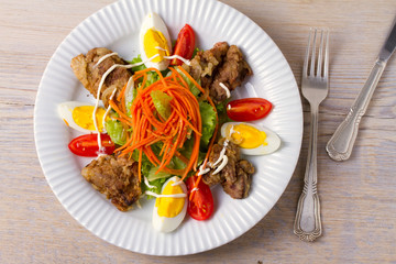 Liver salad with carrot, eggs, tomatoes and lettuce on white plate