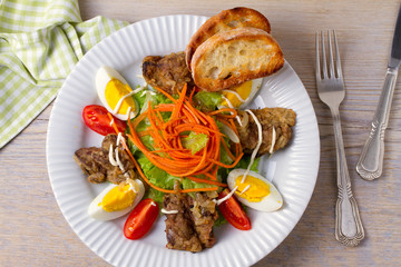Liver salad with carrot, eggs, tomatoes and lettuce on white plate