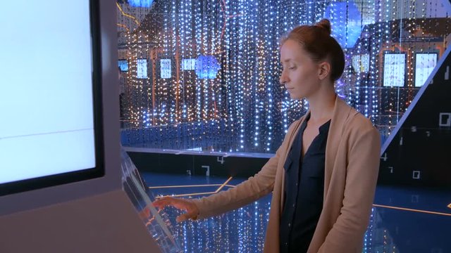 Woman using interactive touchscreen stand and watching video presentation on large display at technology exhibition with futuristic interior