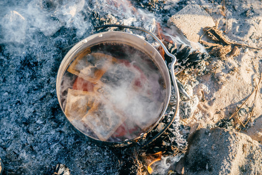 Boiling water in metal pot outdoors. Tea preparation in wild nature in camping trip. Tourist equipment. Cooking in travel on bonfire with firewoods. Adventure in Portugal. Food and drinks in morning.