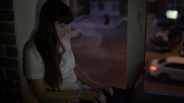 A business woman sits on the windowsill and rejoices at the successful completion of the deal evening, outside the window in the street a road with a busy traffic.