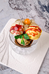Top view of Dessert - Three balls of multi flavor ice cream with Scoops of Chocolate, Vanilla and Fruit Ice Cream with Fresh Mint in Glass Dish on a white plate on a gray background.