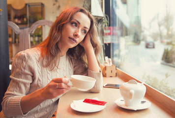 Thoughtful woman having coffee alone