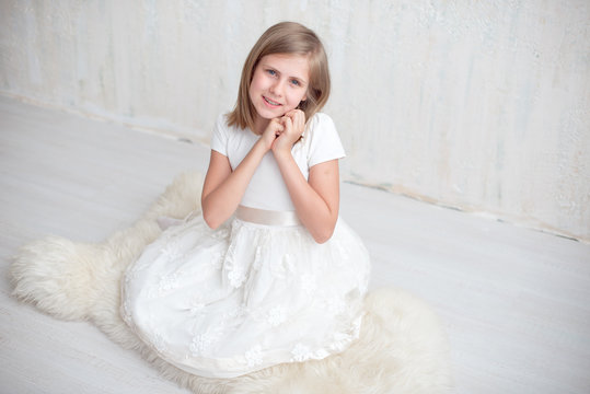 Pretty grade-schooler girl in white dress sitting on the floor.