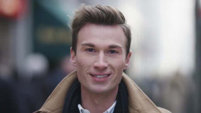 Portrait of handsome young caucasian male smiling to camera in a busy high street, in slow motion
