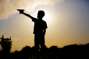 Happy kid playing with paper airplane in the sunset. Silhouette of a child. Ecology.